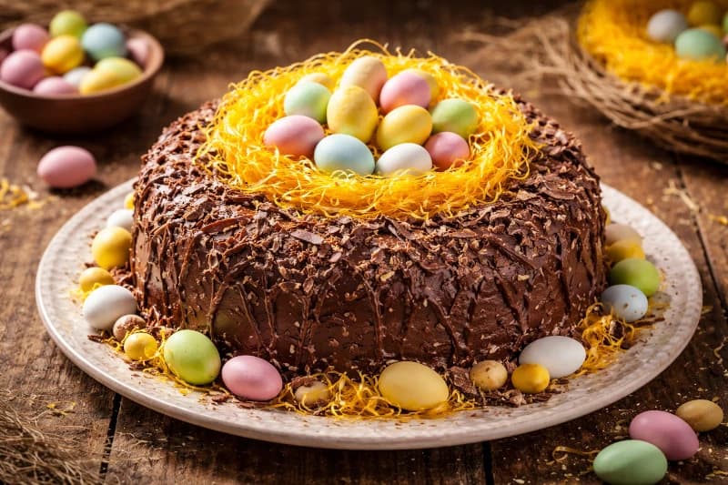 Bolo fofo com cobertura cremosa de chocolate, finalizado com fios de ovos e amêndoas coloridas, perfeito para a mesa de Páscoa.